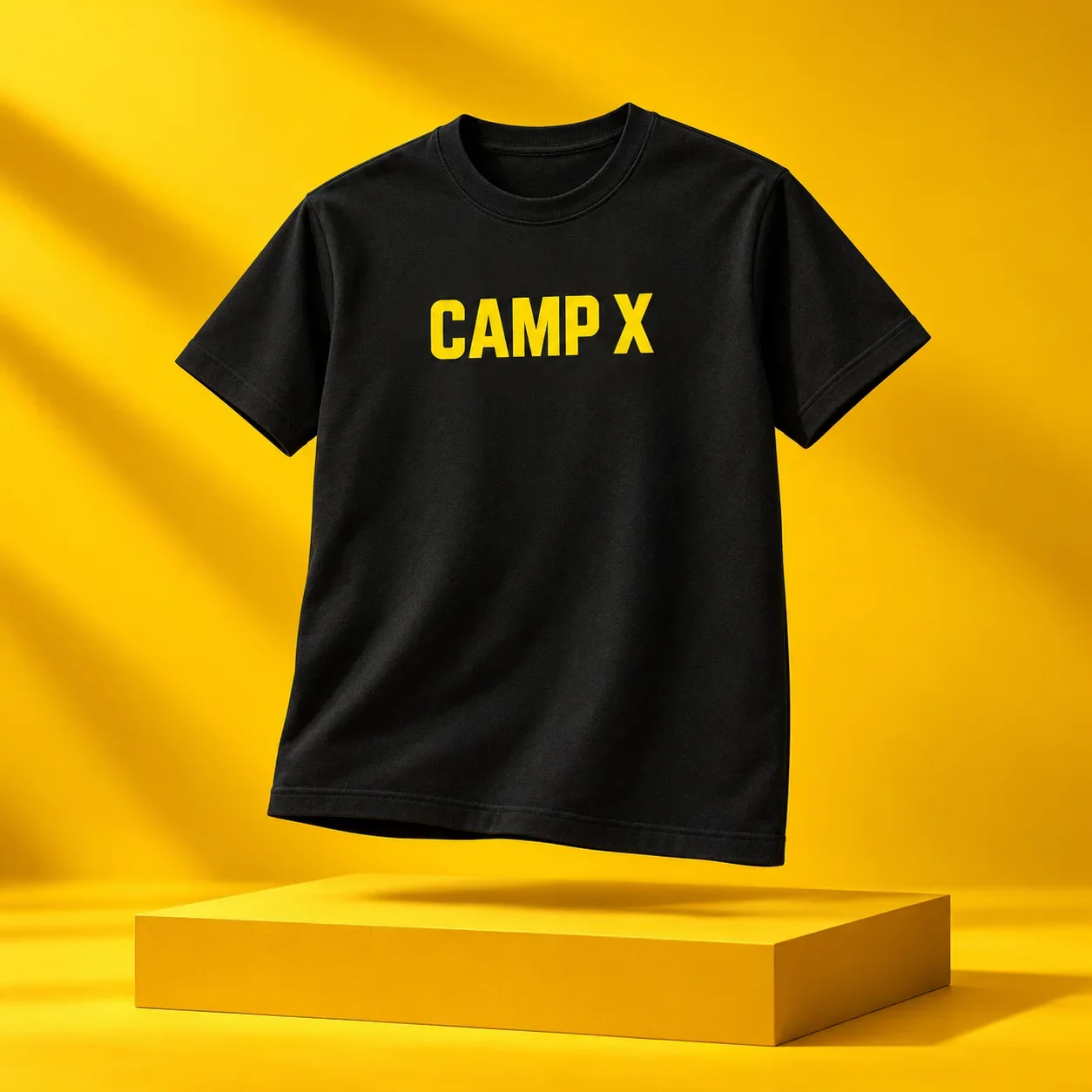 Black T-shirt with yellow CAMP X lettering floating above a yellow display plinth on a yellow background